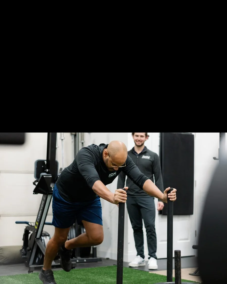 Client pushing a weighted sled with a coach in the iON gym